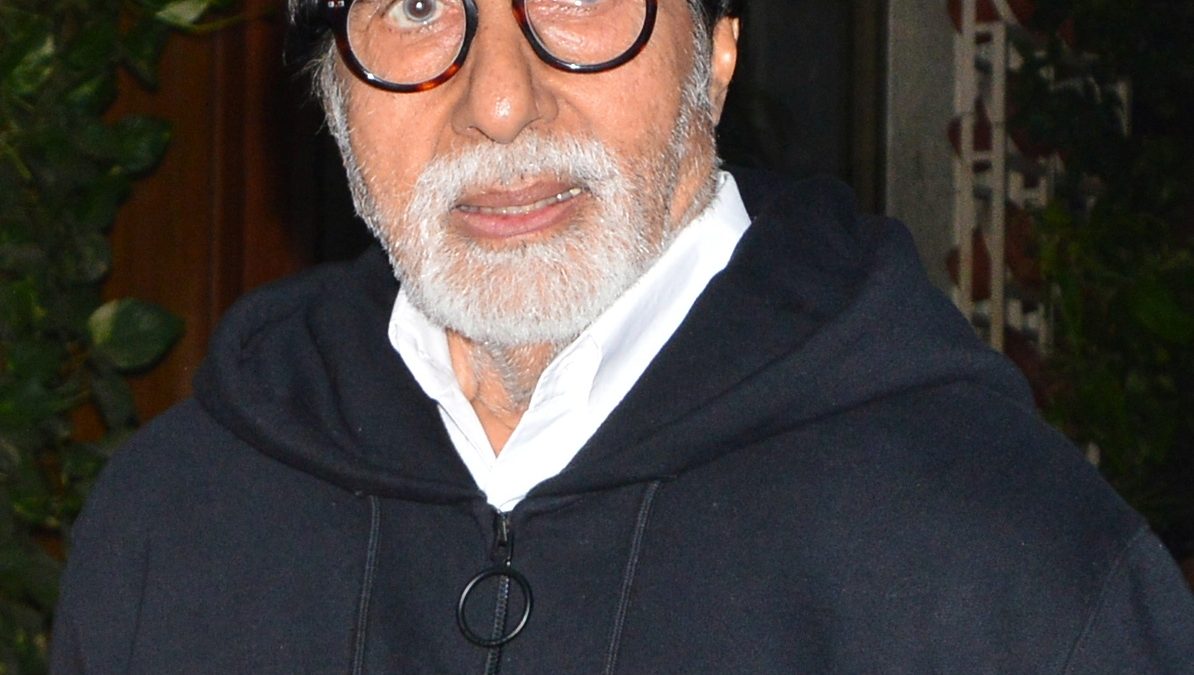 Amitabh Bachchan with a white beard and black-rimmed glasses wearing a dark hooded jacket