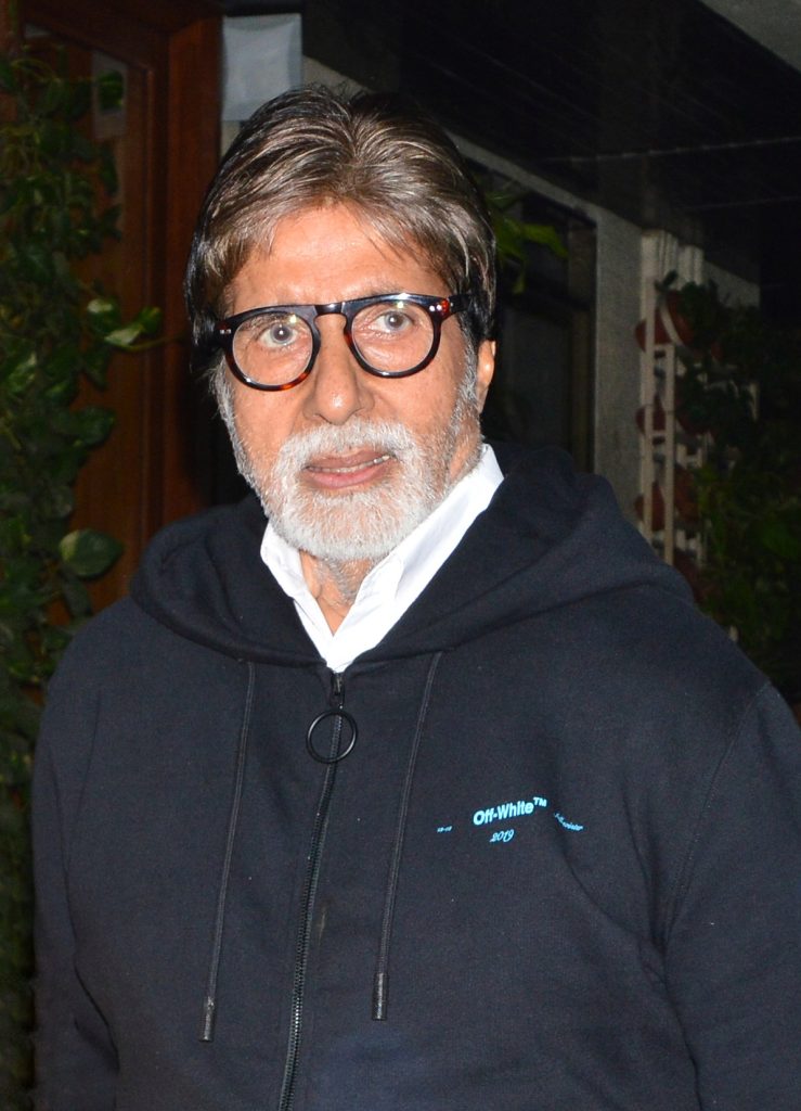 Amitabh Bachchan with a white beard and black-rimmed glasses wearing a dark hooded jacket