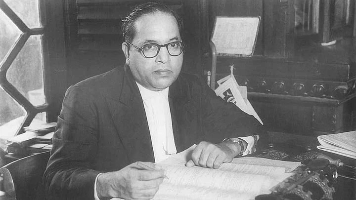 Black-and-white photo of B. R. Ambedkar seated at his desk with papers