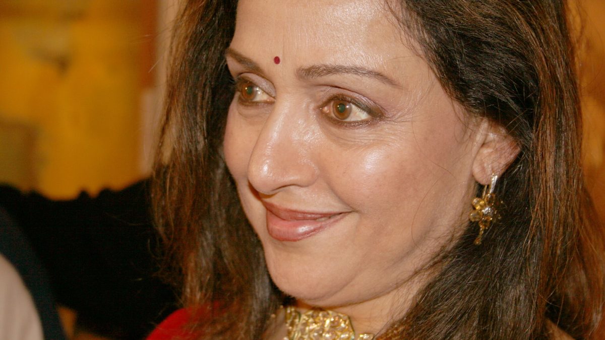 Hema Malini smiling in a red outfit and gold choker at an event in Kolkata