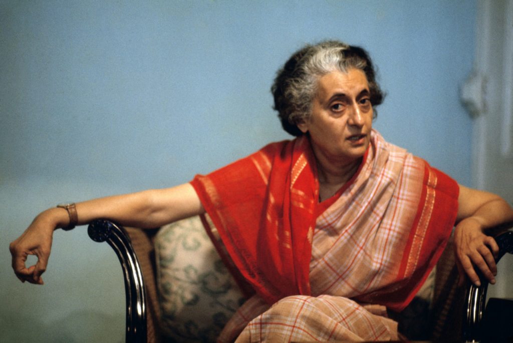 Indira Gandhi in a red and orange sari seated in a chair