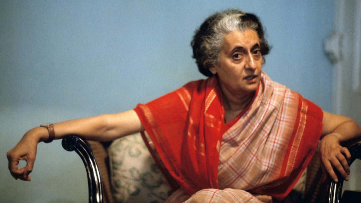 Indira Gandhi in a red and orange sari seated in a chair