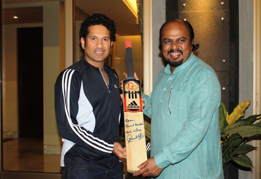 Sachin Tendulkar holding a signed cricket bat with artist Pramod Kamble
