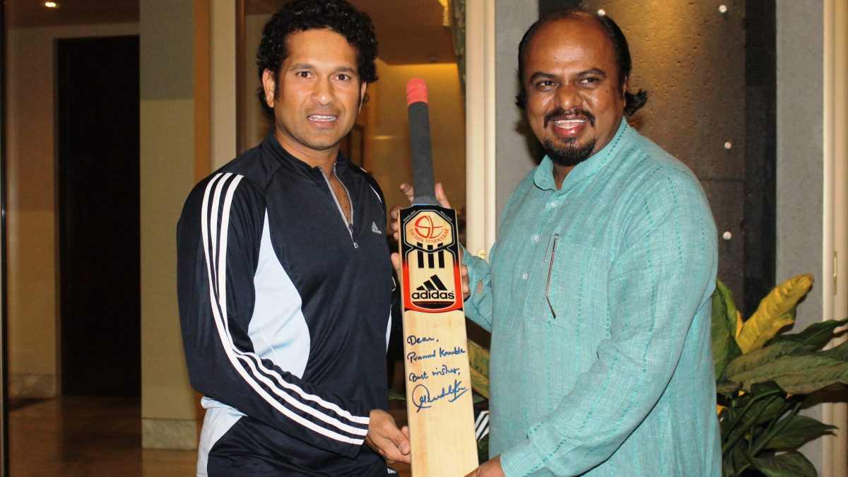 Sachin Tendulkar holding a signed cricket bat with artist Pramod Kamble