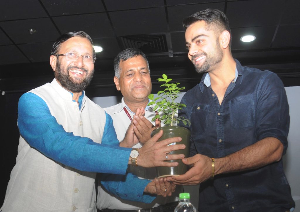 Virat Kohli smiling while holding a potted plant with Union Minister Prakash Javadekar