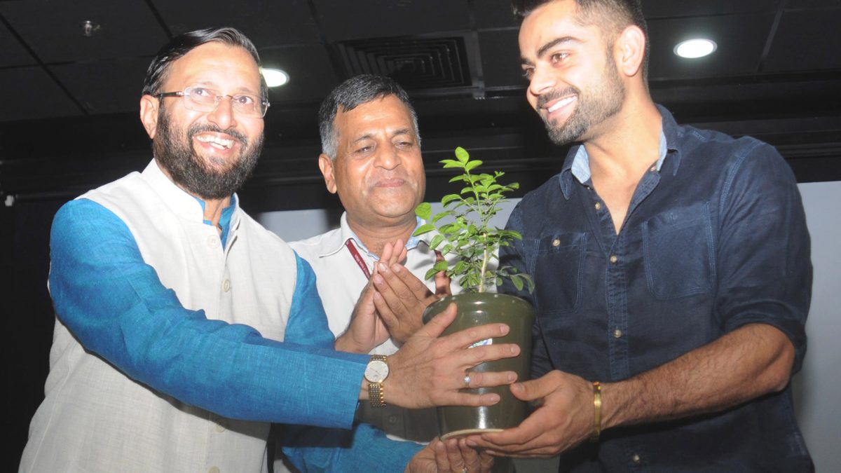 Virat Kohli smiling while holding a potted plant with Union Minister Prakash Javadekar