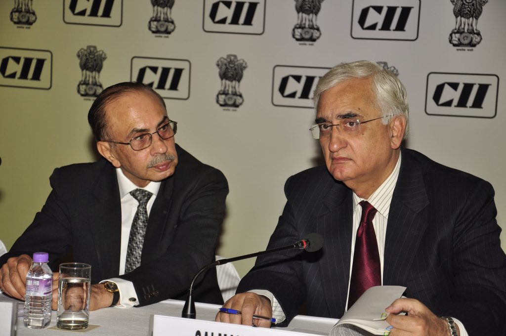 Adi Godrej in glasses and a dark suit seated beside External Affairs Minister Salman Khurshid at a conference