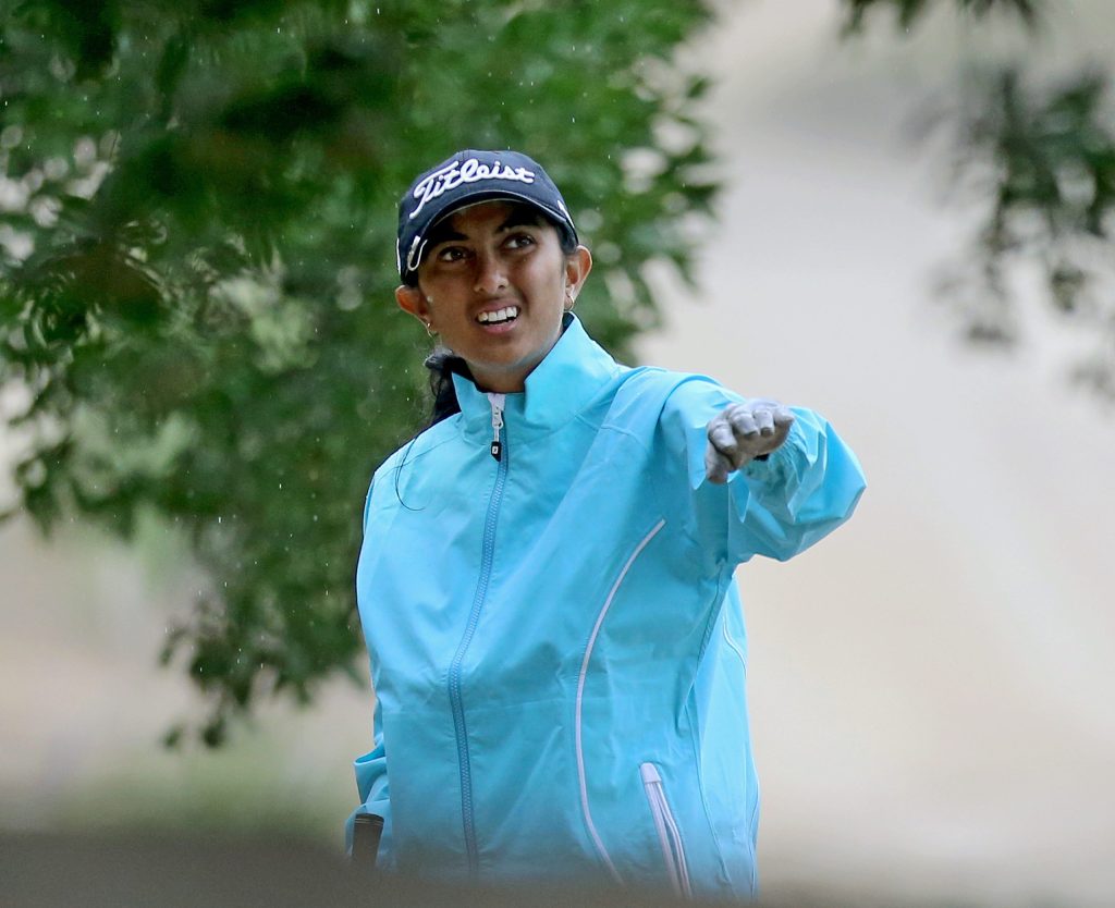 Aditi Ashok in a blue jacket and cap pointing down the course