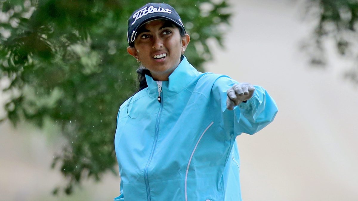 Aditi Ashok in a blue jacket and cap pointing down the course