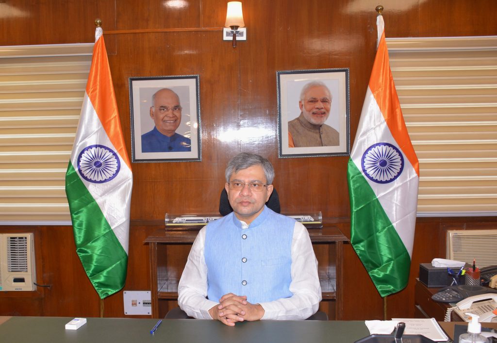 Ashwini Vaishnaw seated at a desk between two national flags