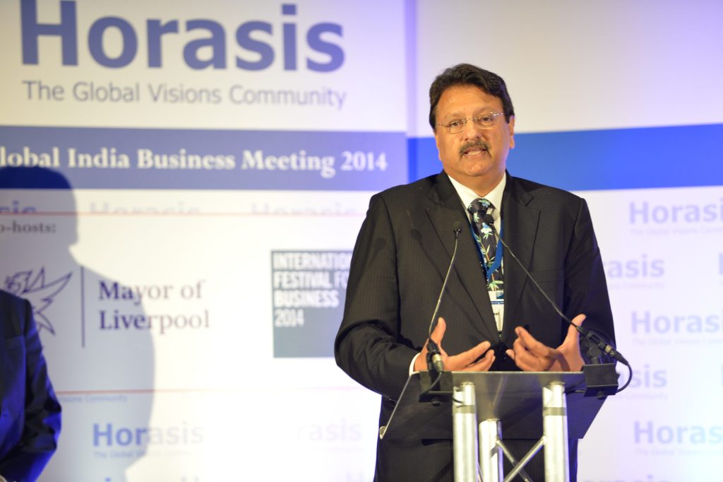 Ajay Piramal in a dark suit and red tie speaking with hands raised