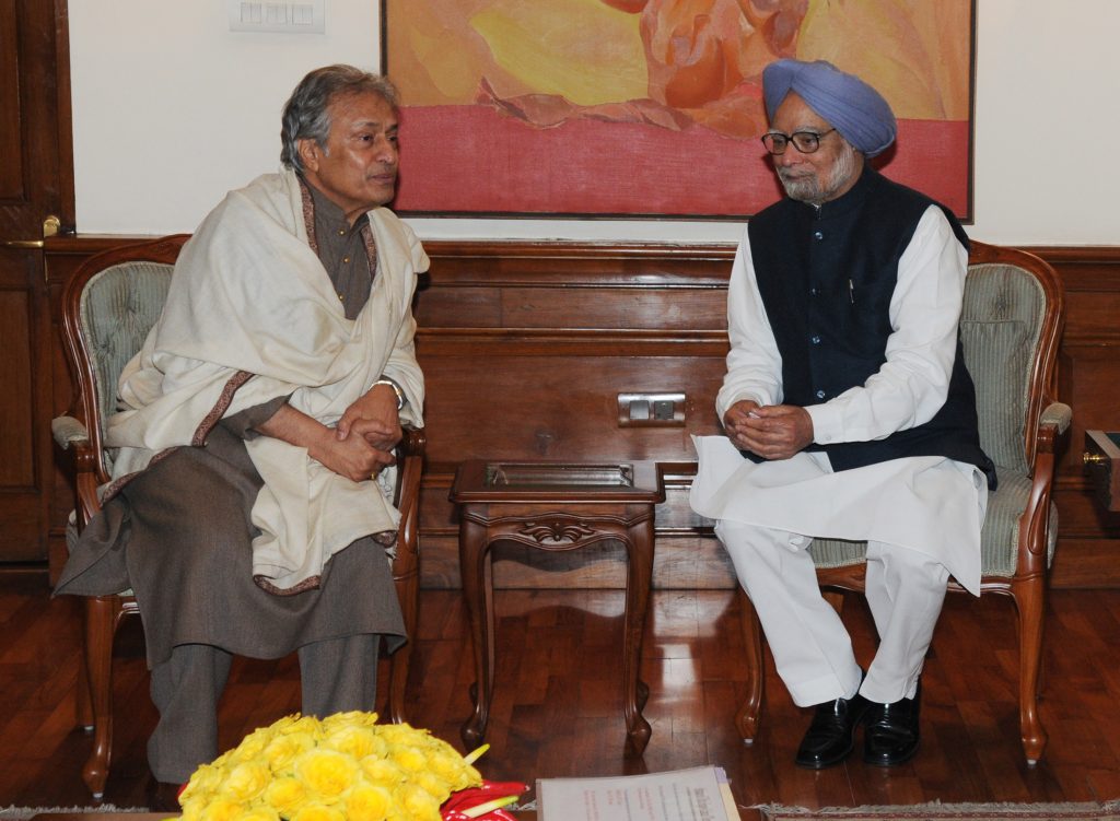 Amjad Ali Khan in a white kurta and shawl seated in conversation with Prime Minister Manmohan Singh