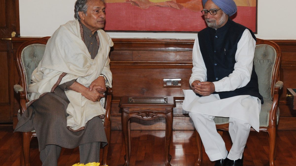 Amjad Ali Khan in a white kurta and shawl seated in conversation with Prime Minister Manmohan Singh