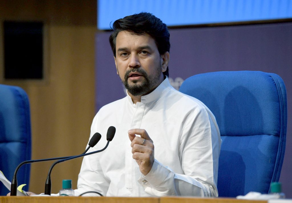 Anurag Thakur in a white kurta speaking at a desk with microphones