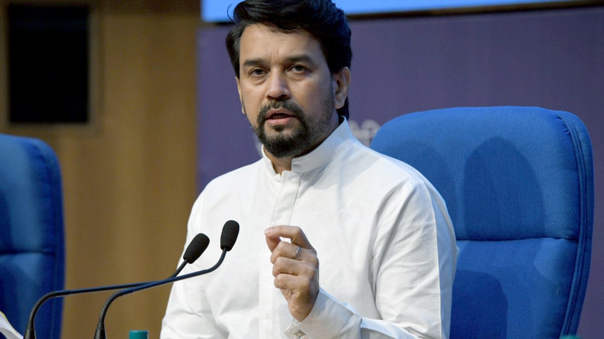 Anurag Thakur in a white kurta speaking at a desk with microphones