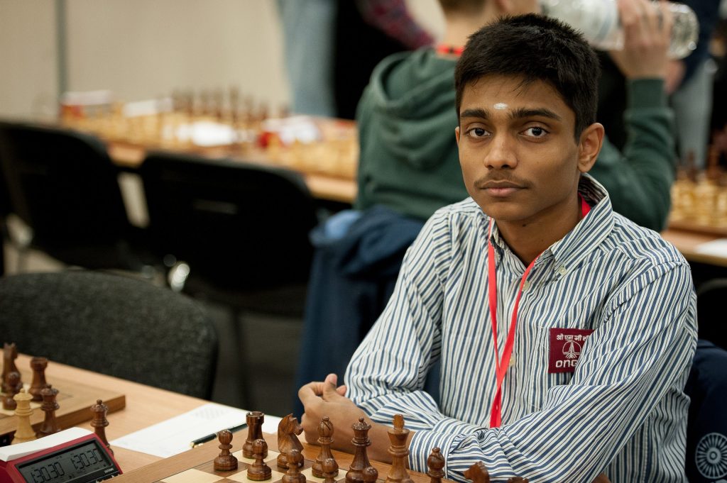 A teenage Aravindh Chithambaram in a striped shirt seated at a chessboard