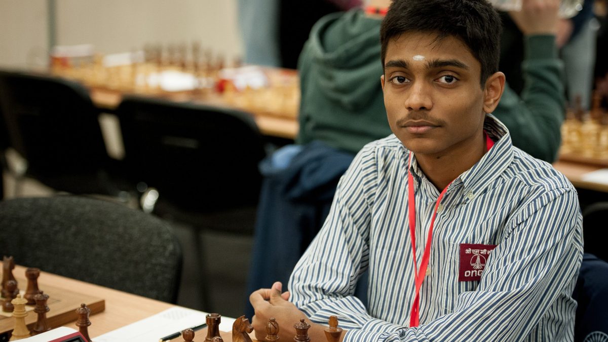 A teenage Aravindh Chithambaram in a striped shirt seated at a chessboard