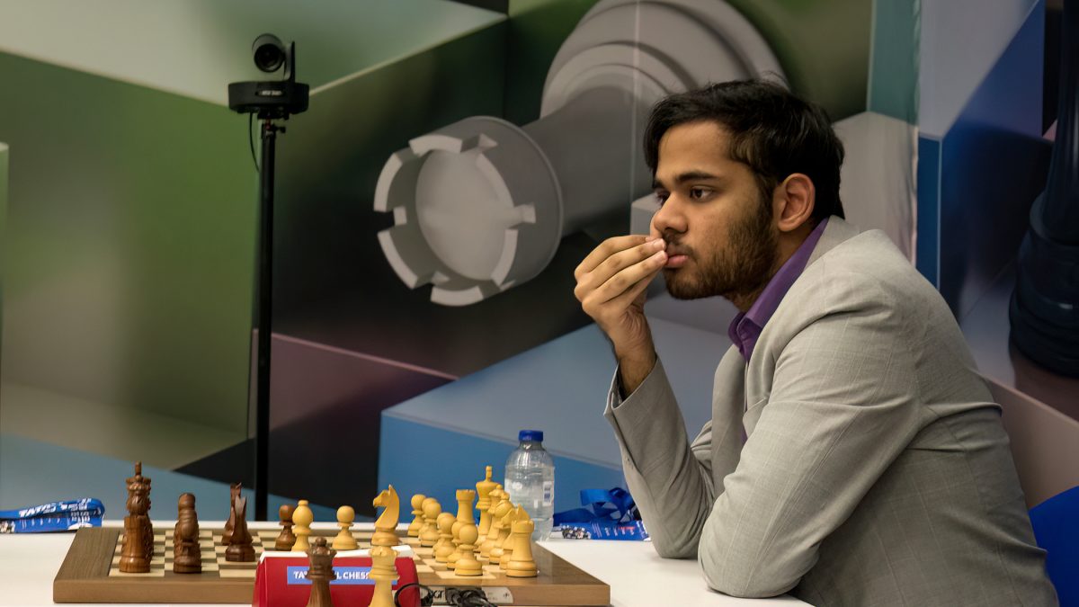 Arjun Erigaisi in a grey jacket thinking at a chessboard with his hand to his mouth