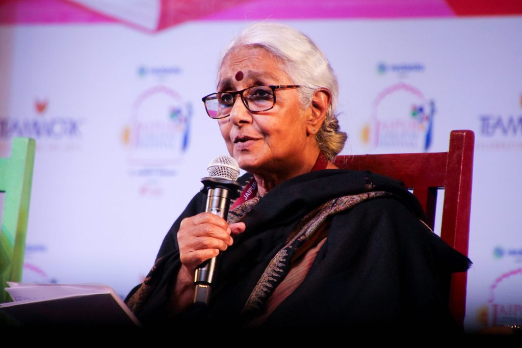 Aruna Roy with grey hair and glasses speaking into a microphone