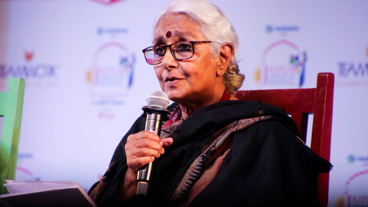 Aruna Roy with grey hair and glasses speaking into a microphone