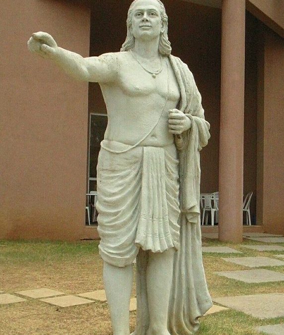 A white stone statue of Aryabhata standing with one arm raised