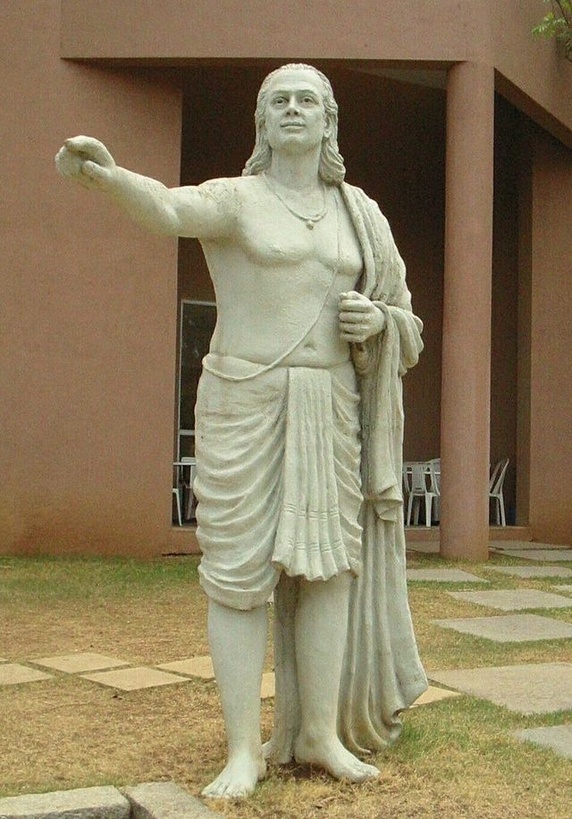 A white stone statue of Aryabhata standing with one arm raised