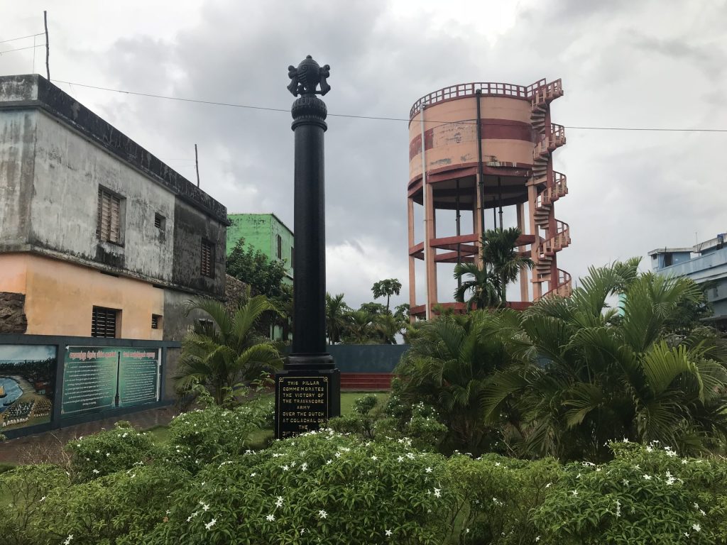 A tall stone victory pillar standing in a garden at Colachel in Tamil Nadu