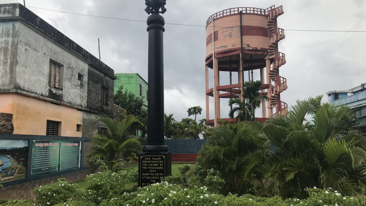 A tall stone victory pillar standing in a garden at Colachel in Tamil Nadu