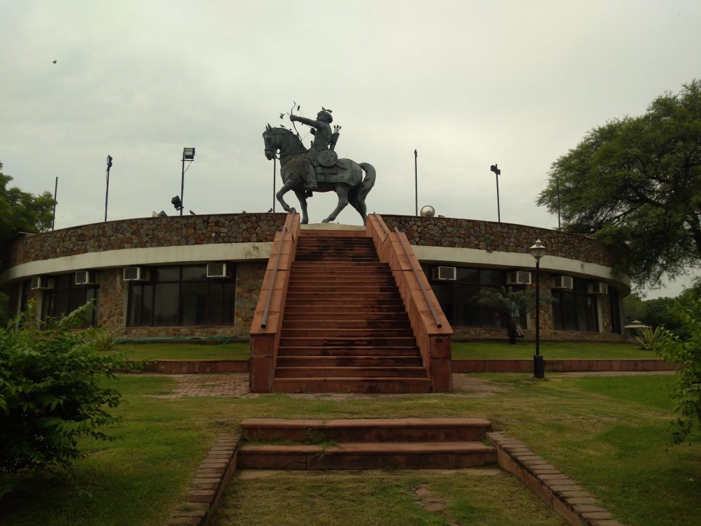 An equestrian statue of Prithviraj Chauhan drawing a bow, on a tall plinth in a park at Qila Rai Pithora in Delhi