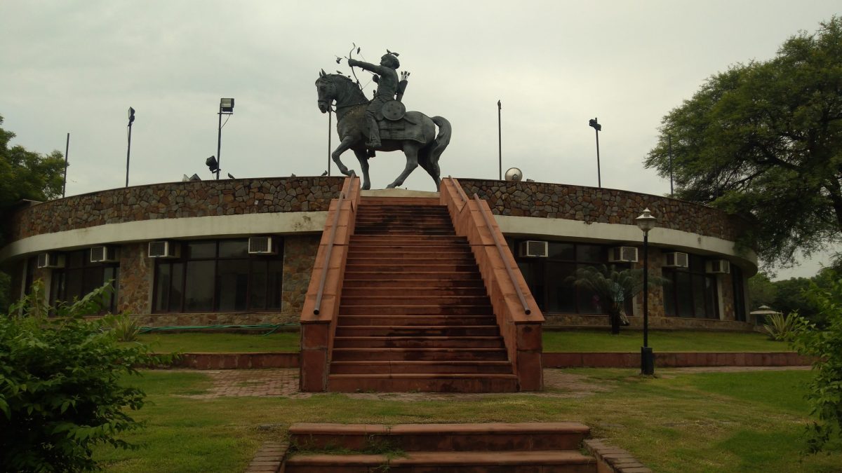 An equestrian statue of Prithviraj Chauhan drawing a bow, on a tall plinth in a park at Qila Rai Pithora in Delhi