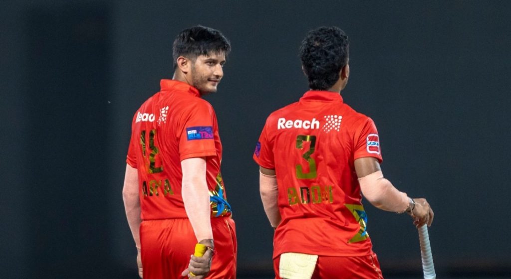 Two batters in red Delhi jerseys with the names Arya and Badoni on their backs