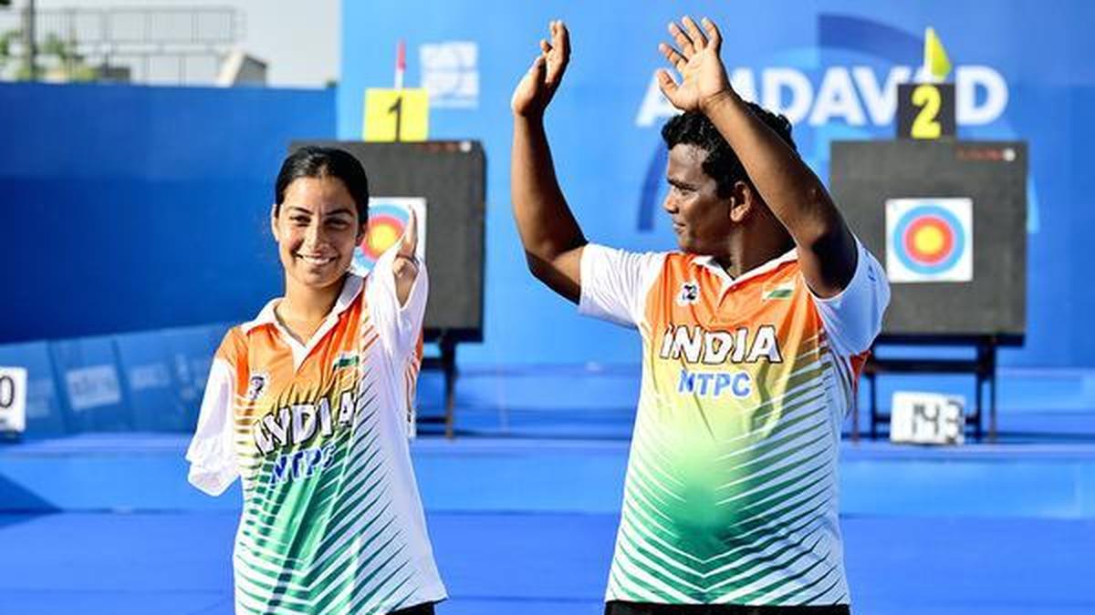 Two Indian para archers in India jerseys waving to the crowd at a competition