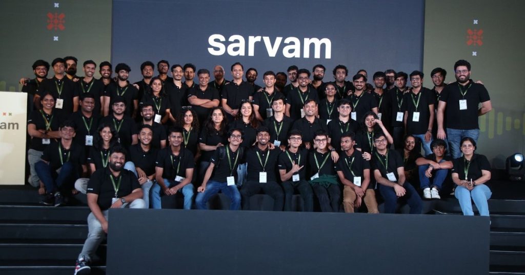 A large group of people in black t-shirts posing on a stage in front of a Sarvam sign