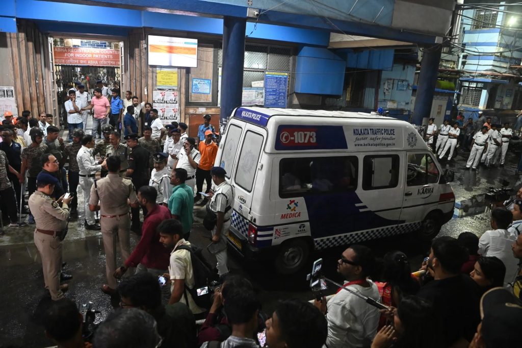 Police and onlookers crowd around a Kolkata Police vehicle outside a hospital entrance at night