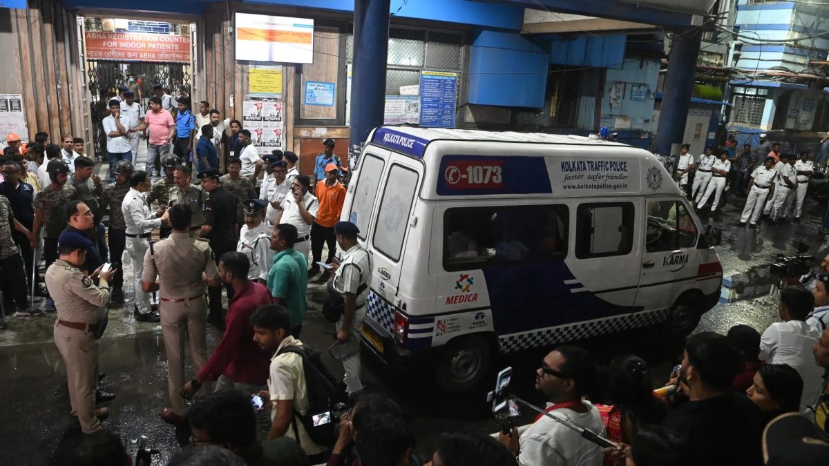 Police and onlookers crowd around a Kolkata Police vehicle outside a hospital entrance at night