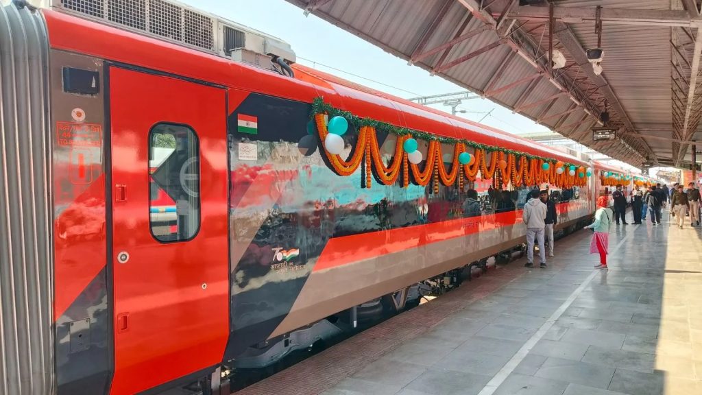 A red Vande Bharat sleeper coach decorated with marigold garlands at a railway platform