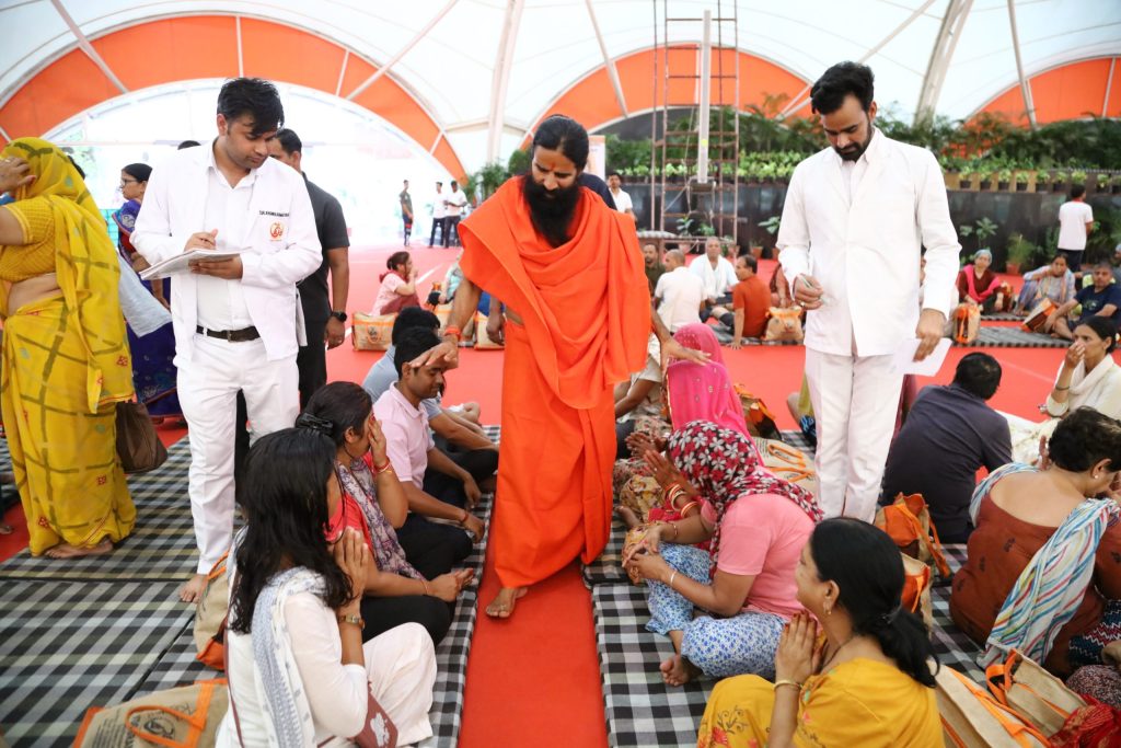 Baba Ramdev in saffron robes walking among followers at a yoga centre