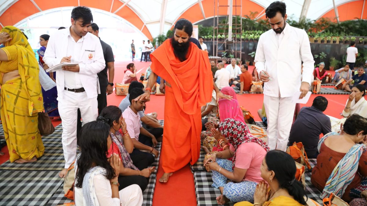 Baba Ramdev in saffron robes walking among followers at a yoga centre
