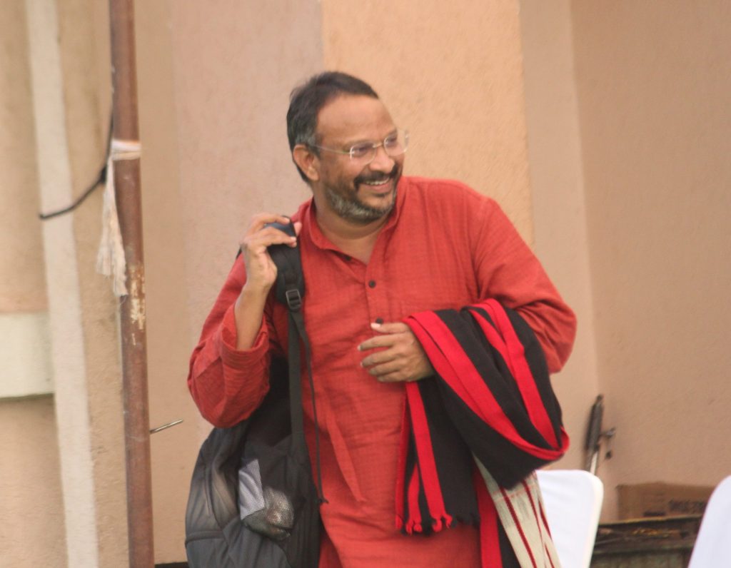 Bezwada Wilson in a red kurta smiling, with a bag over his shoulder