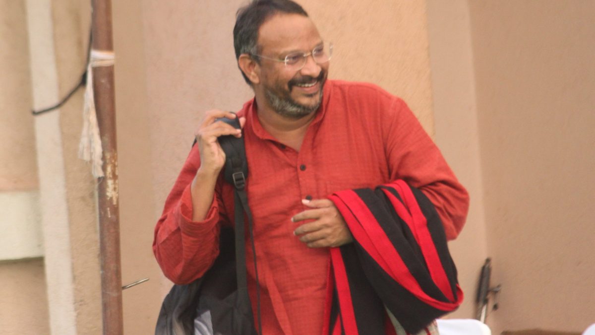 Bezwada Wilson in a red kurta smiling, with a bag over his shoulder