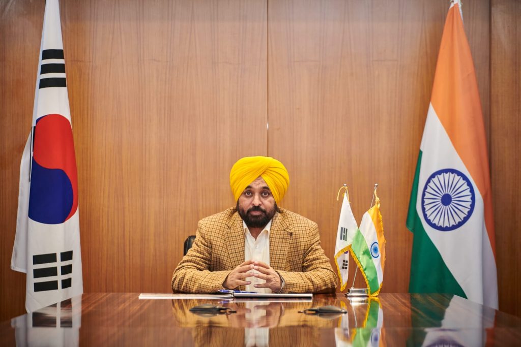 Bhagwant Mann in a yellow turban seated at a desk between the South Korean and Indian flags