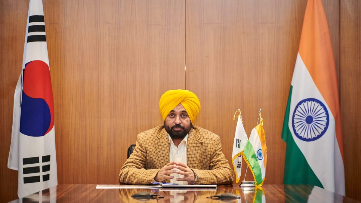 Bhagwant Mann in a yellow turban seated at a desk between the South Korean and Indian flags