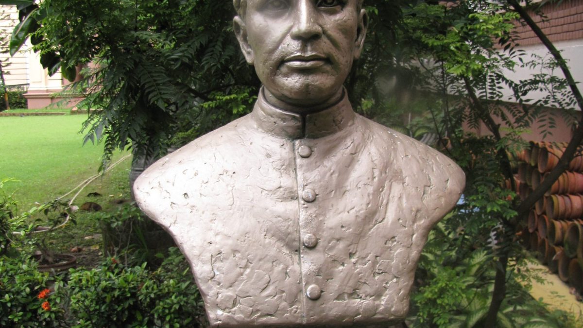 A stone bust of Birbal Sahni wearing a cap, set on a pedestal in a garden