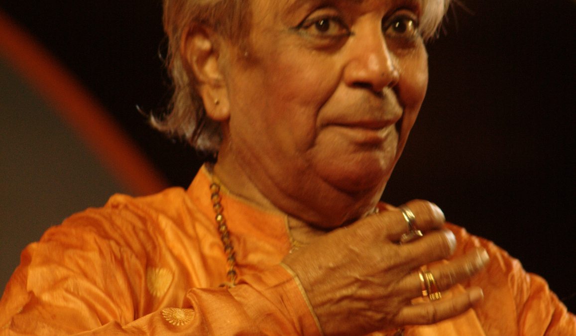 Birju Maharaj in an orange kurta, mid-gesture during a Kathak performance