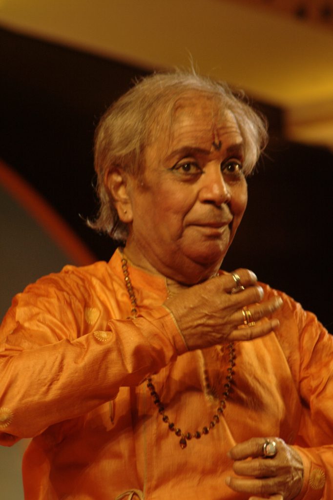 Birju Maharaj in an orange kurta, mid-gesture during a Kathak performance