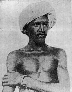 A black-and-white photograph of Birsa Munda in a turban, arms folded