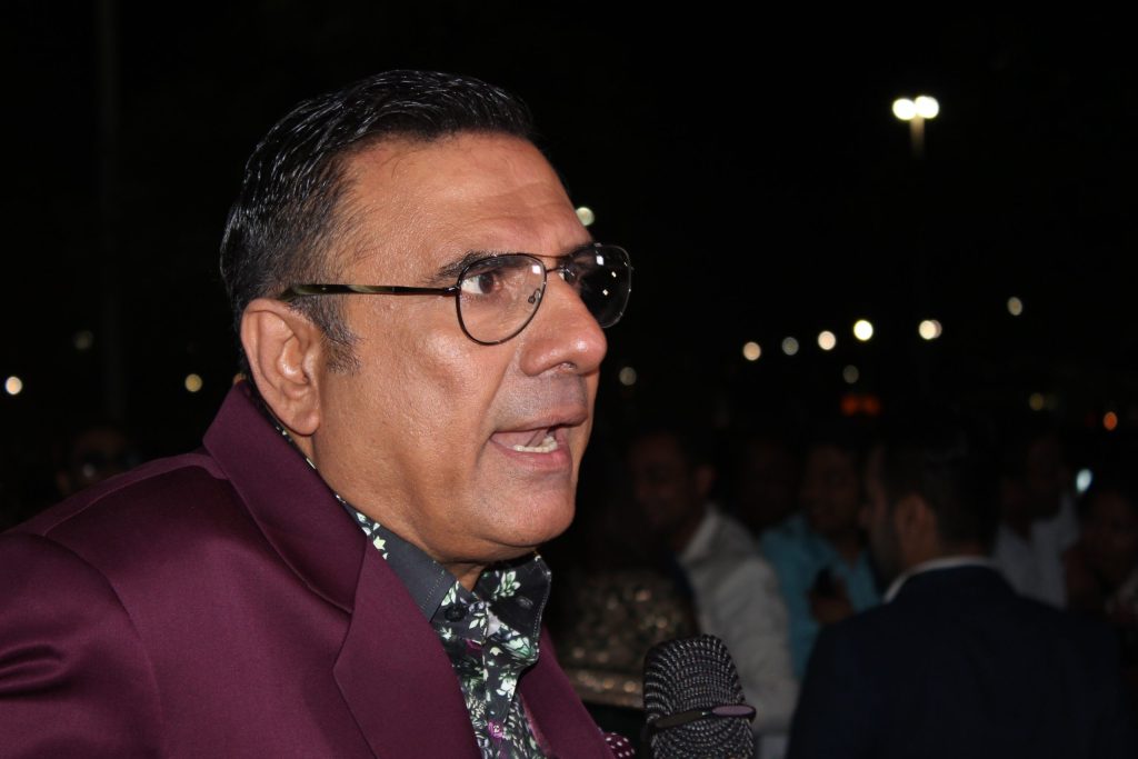 Boman Irani in glasses and a maroon velvet jacket speaking on the green carpet at night
