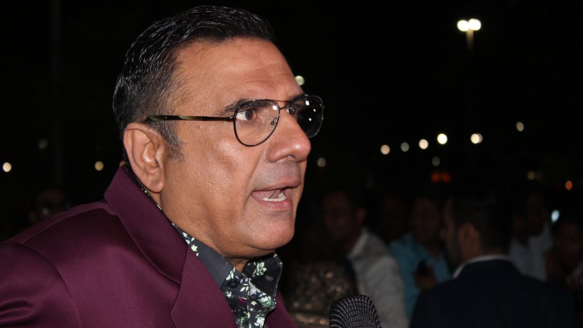 Boman Irani in glasses and a maroon velvet jacket speaking on the green carpet at night