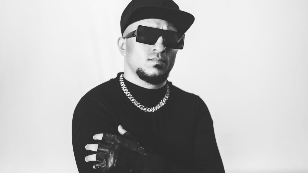 Black and white photo of Brodha V in a cap, sunglasses and chain with his arms crossed