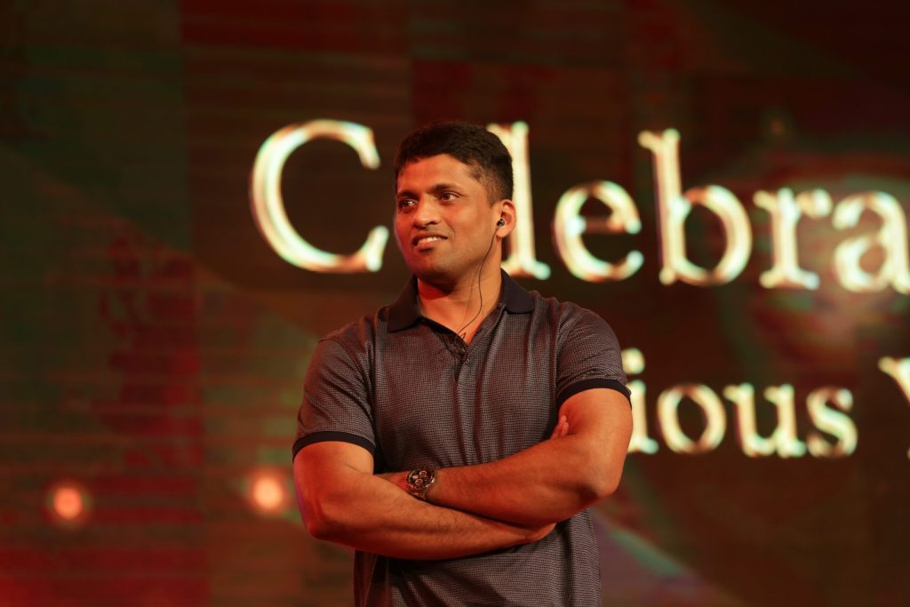 Byju Raveendran in a dark polo shirt standing with arms crossed on a stage